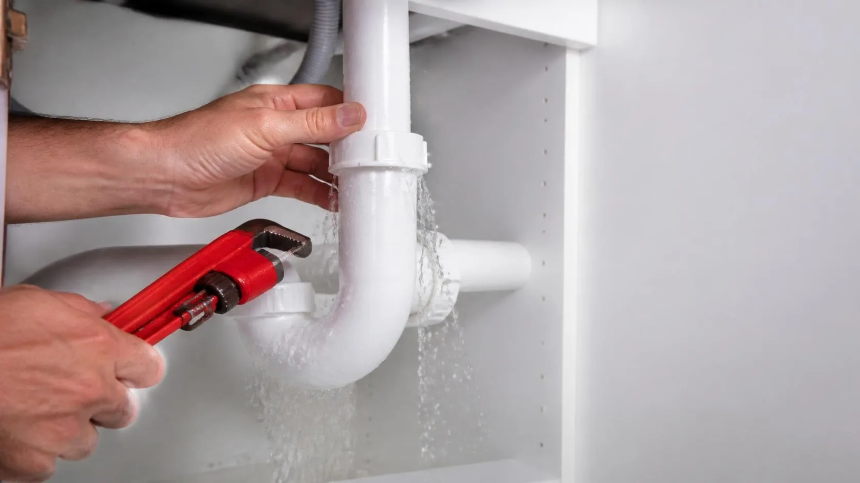 Plumber repairing a leaking pipe under a sink in Worthing